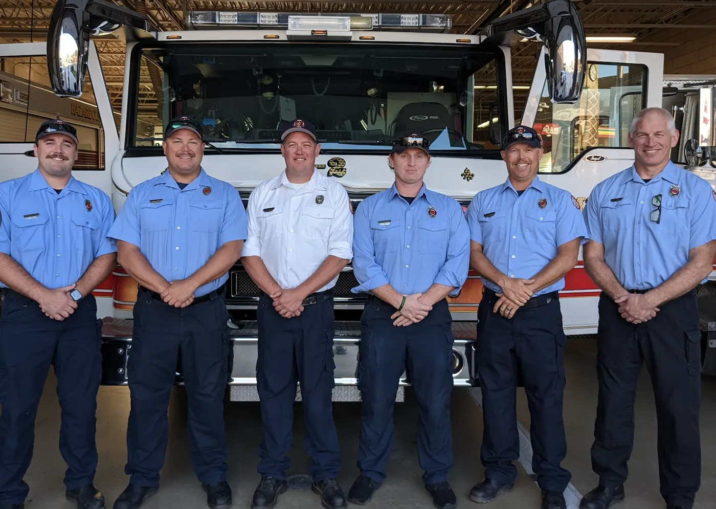Six firefighters standing in front of a fire engine in the station bay
